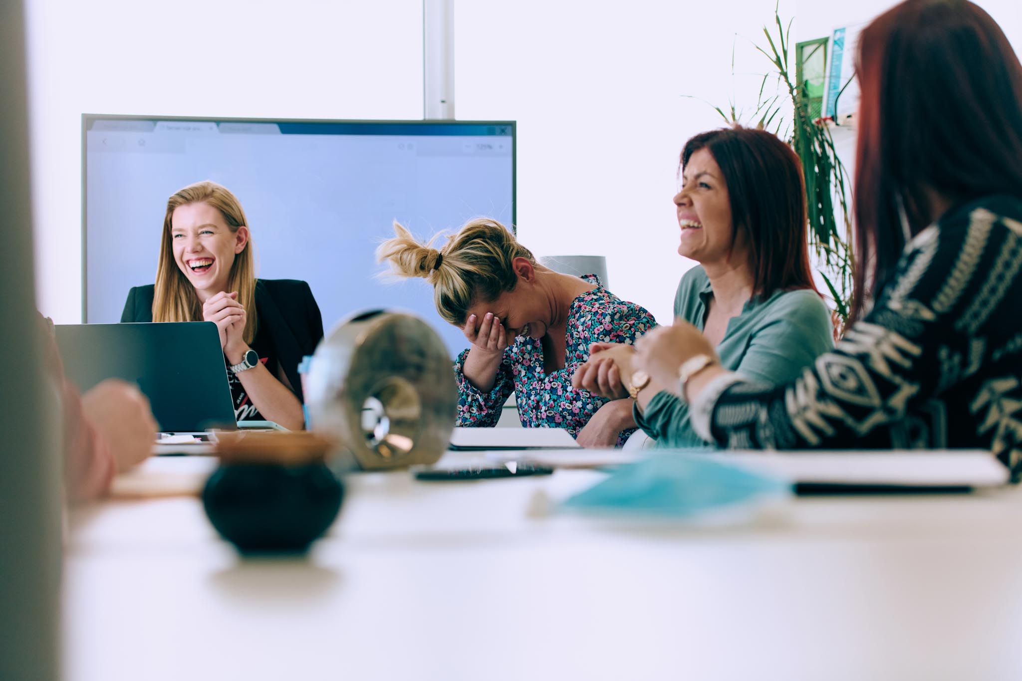 A diverse team of business professionals engaged in a discussion about projects in a modern glass walled office.